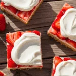 A close-up of delicious Strawberry Shortcake Bars on a white plate, garnished with fresh strawberries and mint leaves.