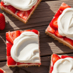 A close-up of delicious Strawberry Shortcake Bars on a white plate, garnished with fresh strawberries and mint leaves.