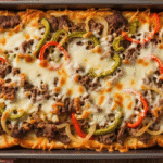 A close-up of a golden brown Philly cheesesteak grilled cheese casserole in a baking dish, with gooey melted cheese and tender beef peeking through the crispy bread.