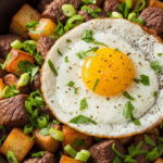 A close-up of a sizzling Steak and Potato Breakfast Hash in a cast iron skillet with eggs, crispy potatoes, and tender steak.