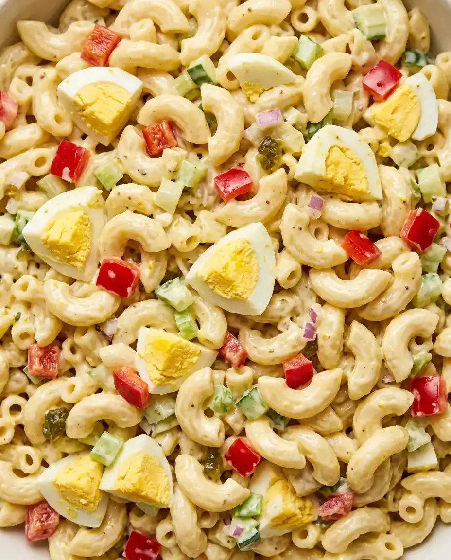 Overhead close-up of creamy Amish macaroni salad with hard-boiled eggs, red pepper, and celery in tangy dressing