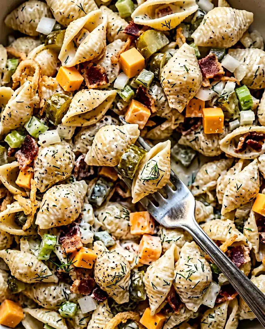 Fork lifting a bite of creamy dill pickle pasta salad showing pickles, cheddar, and bacon in warm light